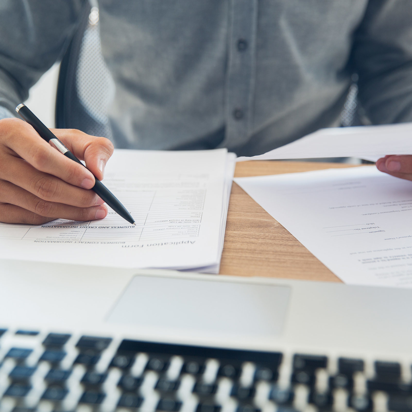 Nebenkosten im Mietvertrag: Mann mit Stift in der Hand sitzt vor einem Laptop und mehreren Dokumenten