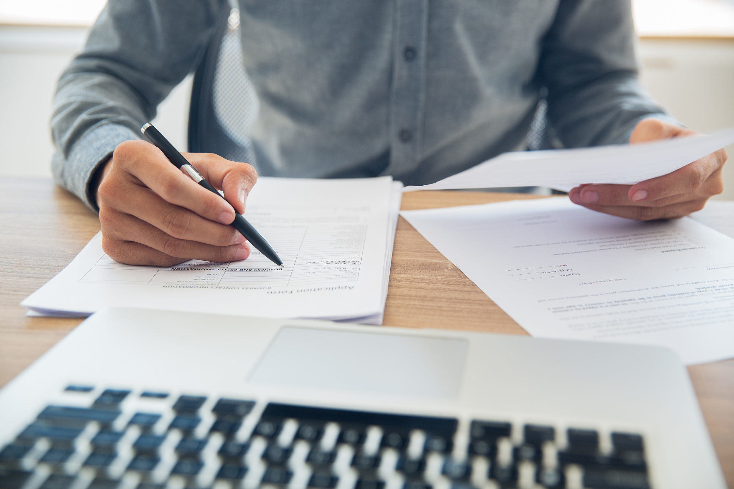 Nebenkosten im Mietvertrag: Mann mit Stift in der Hand sitzt vor einem Laptop und mehreren Dokumenten