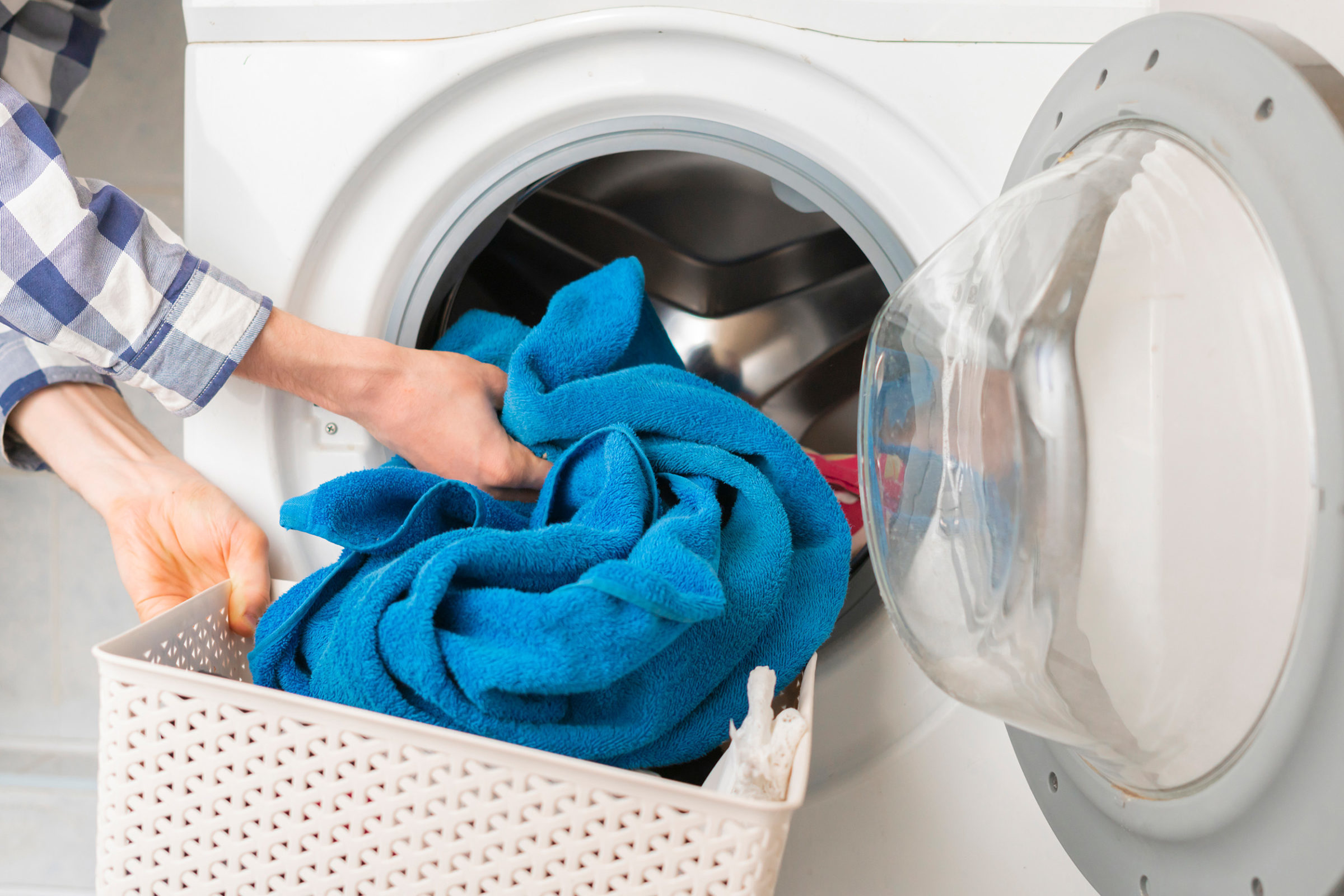 Waschkueche im Mehrfamilienhaus: Befuellen einer Waschmaschine mit einem blauen Handtuch