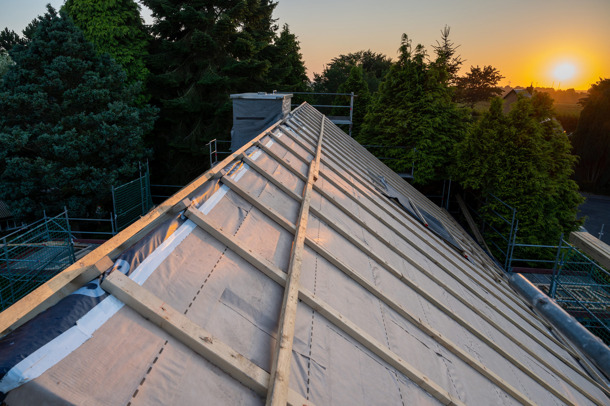 GEG: Ungedecktes Dach mit Holzbalken im Sonnenuntergang. Im Hintergrund sind Baeume.