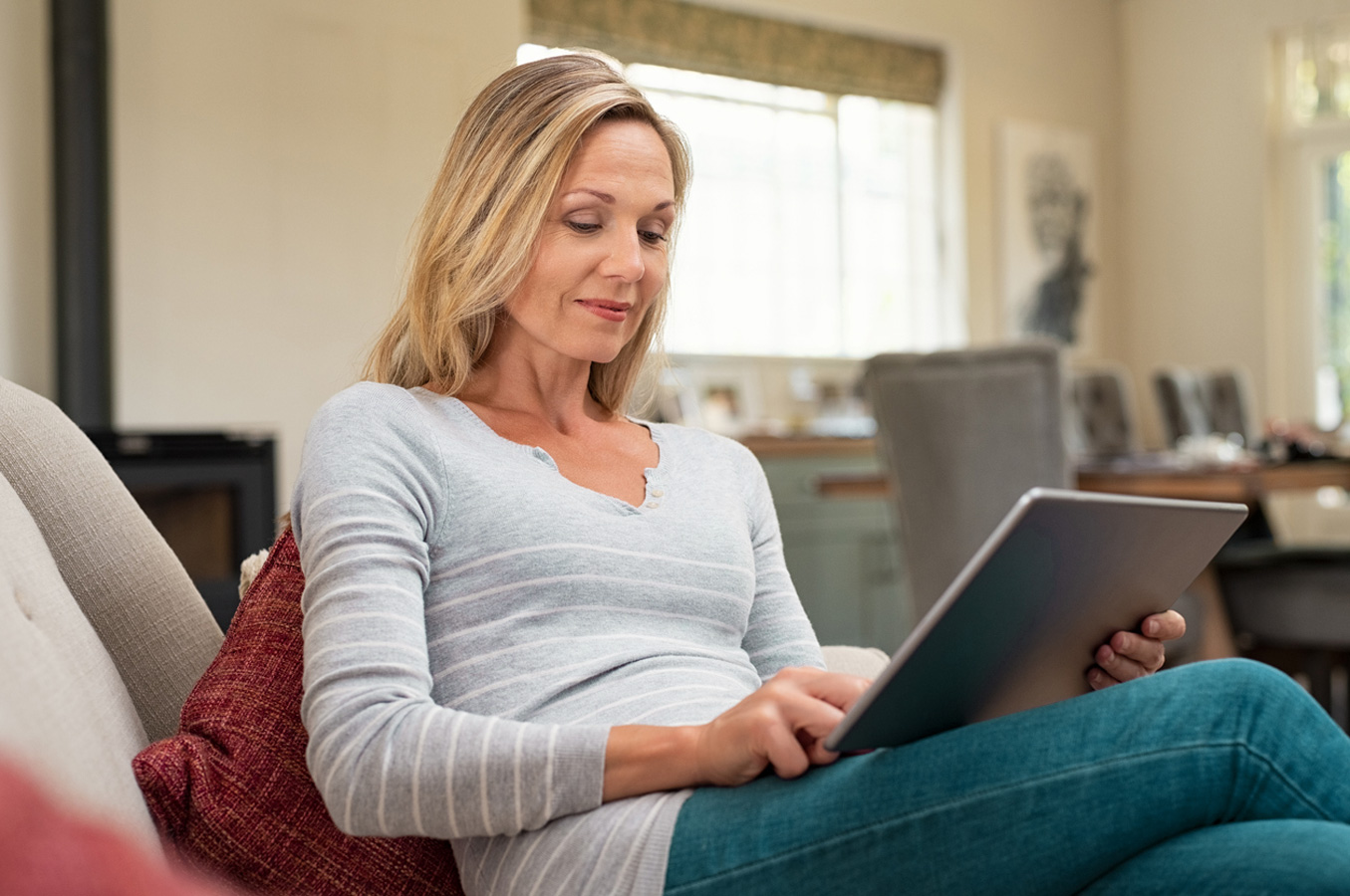 Unterjaehrige Anpassung Nebenkostenvorauszahlung: Frau sitzt auf der Couch und liest etwas auf einem Tablet.