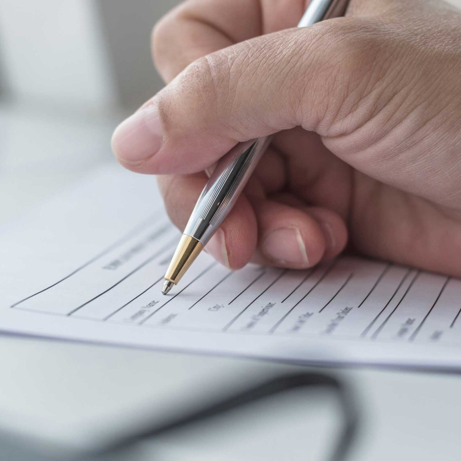 Hand, die einen Stift umfasst, setzt zum Schreiben auf einem Dokument an, das auf einem weißem Tisch liegt.